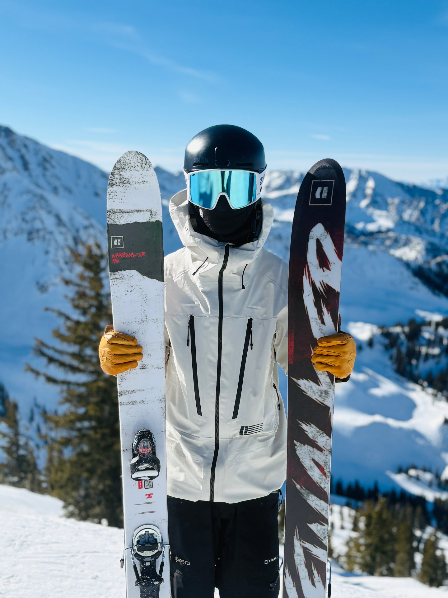 Oskar Lighthiser in a white ski jacket and helmet holding skis against a snow-covered mountain backdrop